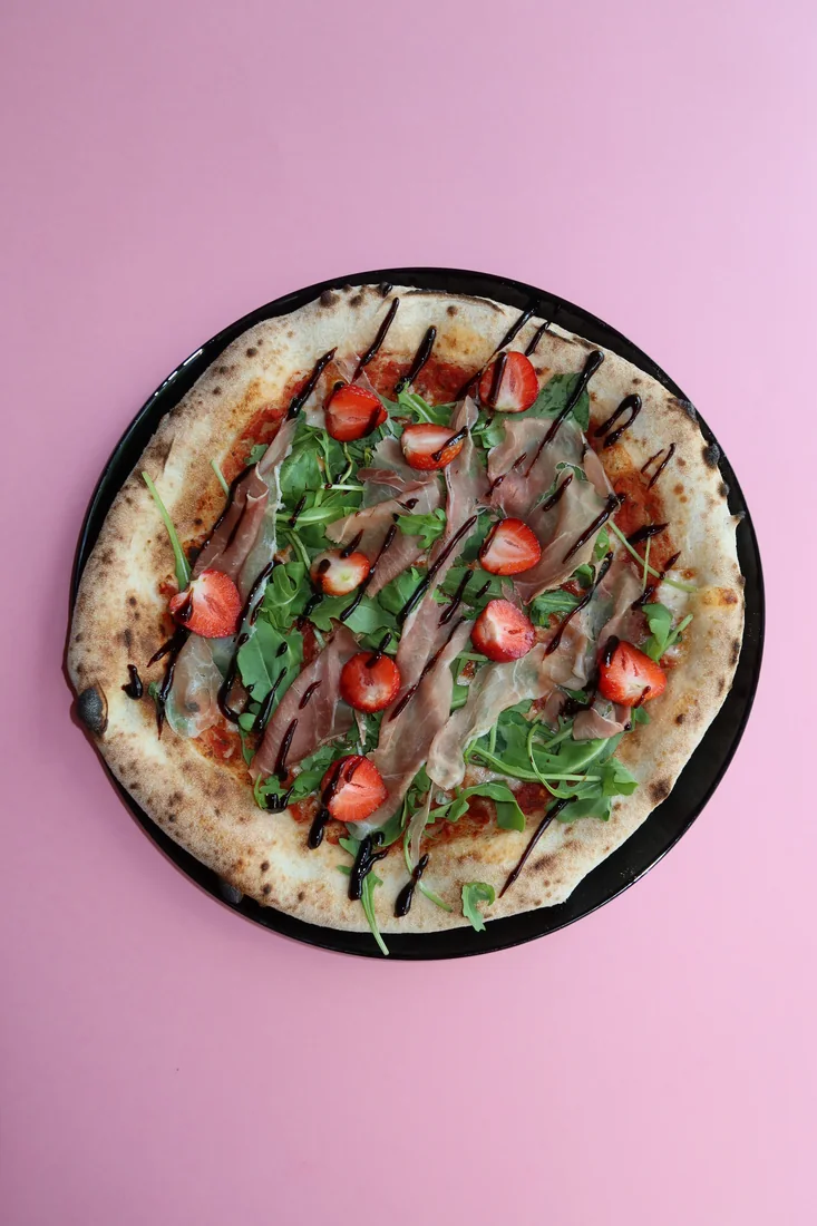 Pizza topped with ham, rocket and strawberries